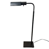 Black adjustable desk lamp on a concrete floor with a white wall background